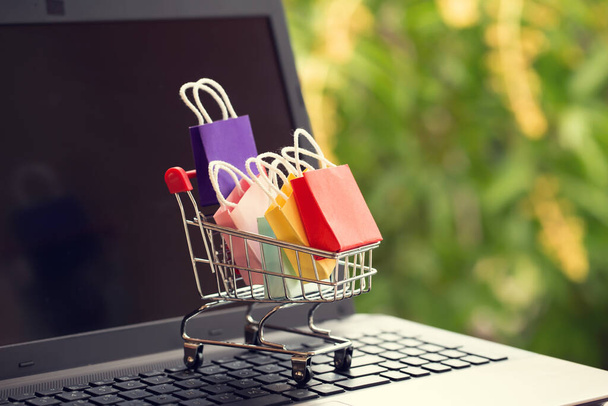 Online-Shopping, E-Commerce-Konzept: Papiereinkaufstaschen im Einkaufswagen oder Einkaufswagen im naturgrünen Hintergrund. Kauf von Produkten im Internet kann Waren aus dem Ausland kaufen - Foto, Bild