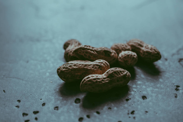 A close-up of a group of whole unpeeled dried peanuts in shell on a concrete blue textured background. A culinary and concept. Natural background.  Copy space. Soft focus - Foto, afbeelding
