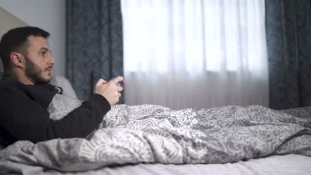 Süchtiger junger Mann spielt Videospiele liegend im Bett - Filmmaterial, Video
