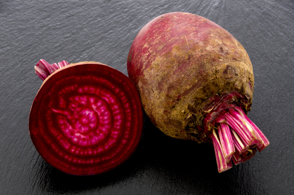 Isolated beet. Whole red beetroot and a half isolated on black stone plate - Photo, Image