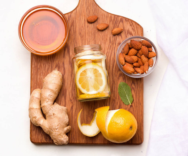 Potje met immuniteitsvriendelijke ingrediënten citroen, amandel, munt en gember op een houten plank. Virusbeschermingsconcept - Foto, afbeelding