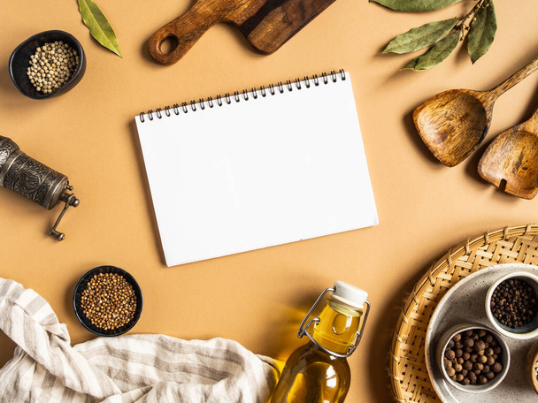 Kitchen flat lay with open notebook for culinary text and small bowls various dry spices, wood kitchen utensils, olive oil in glass bottle on a beige background. Top view. copy space - Foto, afbeelding