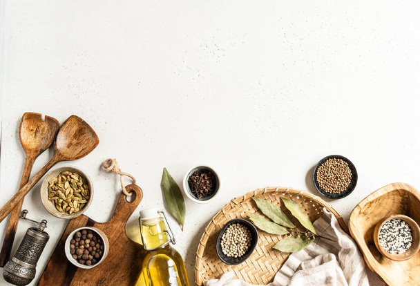 Flat lay of small bowls various dry spices, wood kitchen utensils and olive oil in glass bottle on a light background. Top view. copy space - Zdjęcie, obraz