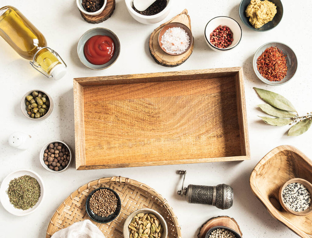 Various dry spices and sauces and wooden tray mock up on a light background. Flat lay of small bowls with dijon mustard, olive oil, ketchup, capers and spices. Copy space. Top view - Photo, Image