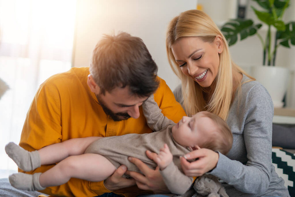 Portrait of a young happy family with the baby at home.Cheerful parents playing with baby boy on bed at home.Love concept. - Foto, Bild