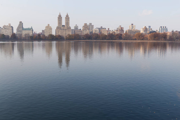 New Yorkin siluetti Central Park järven toisesta päästä, vesi heijastaa taivaanrantaa ja sinistä taivasta
 - Valokuva, kuva