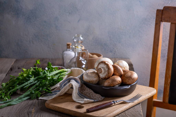 Produkte für die Zubereitung von Pilzgerichten. Champignons, Dill, Petersilie, grüne Zwiebeln auf einem Holztisch. Kochkonzept - Foto, Bild