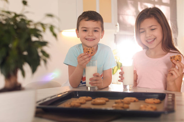 Cute little children eating cookies with milk in kitchen. Cooking pastry - Foto, afbeelding
