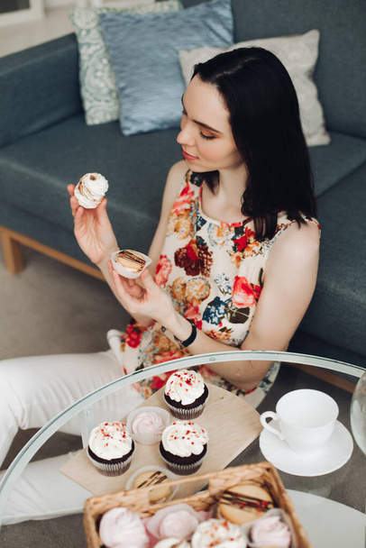 Beautiful woman with marshmallow in hands. She is sitting at coffee table with homemade cupcakes. - Fotó, kép