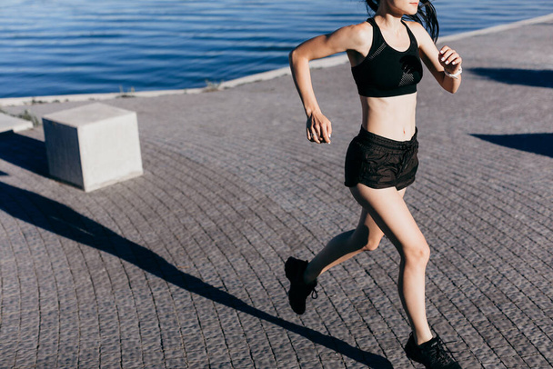 Sabah şehir plajında sabah koşusu yaparken siyah giyinmiş atletik bir kızın fotoğrafı.. - Fotoğraf, Görsel