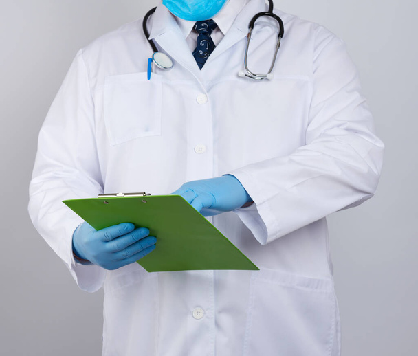 médico con una bata blanca, guantes de látex azul, estetoscopio colgando de su cuello, sosteniendo un portapapeles
  - Foto, Imagen