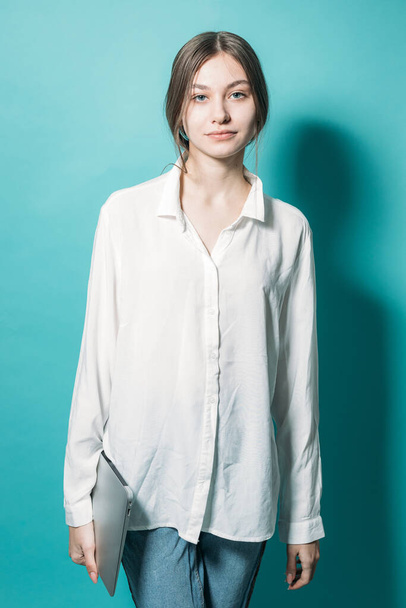 young girl in a white shirt and jeans with a laptop on a blue background in the studio - Foto, immagini