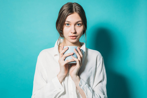 giovane ragazza in camicia bianca e jeans con una tazza di caffè su uno sfondo blu
 - Foto, immagini