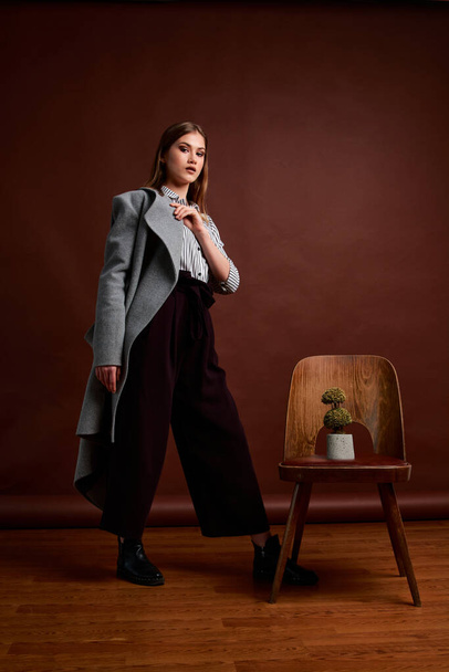 Mininalism style classic studio photo set of the young independent woman. Gorgeous young female in classic suit, black shoes and grey coat. Vintage chair. Woman's clothes. Fashionable clothes. - Фото, зображення