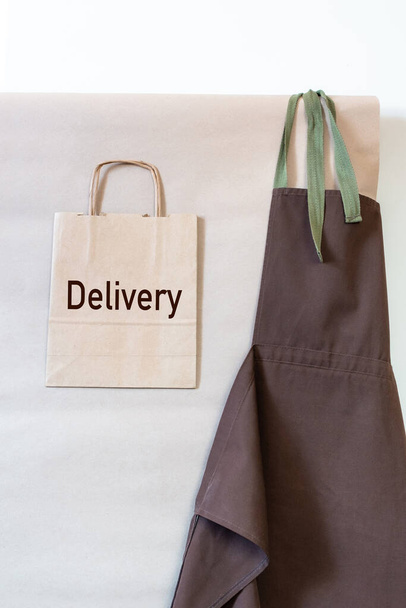 Craft Paper Bags with sign Delivery and brown apron on the wall. Concept of Uniform Delivery Service for Customer. - 写真・画像