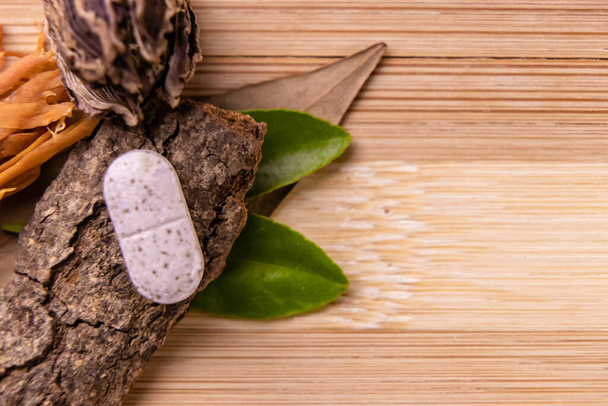 Wide shot of one white herbal tablet placed on an inverted cinnamon stick with dry spices and wooden background. Herbal concept - Foto, afbeelding