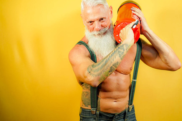 Фитнес-человек показывает свою силу. Модель с белой длинной бородой на жёлтом фоне. Пожилой фитнес и здоровая концепция
 - Фото, изображение