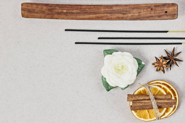 Incense sticks with stand, sliced in orange circles in a wooden bowl and anise star, cinnamon sticks on a gray background.Candle in the form of a flower and a shell.Aromatherapy. Home spa concept - Фото, изображение