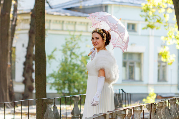 Beautiful girl in a white dress with a pink umbrella on a background of autumn trees close-up - Foto, Imagen
