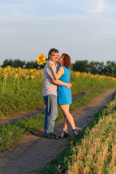 Couple adulte câlinant dans un champ avec des tournesols au coucher du soleil
. - Photo, image