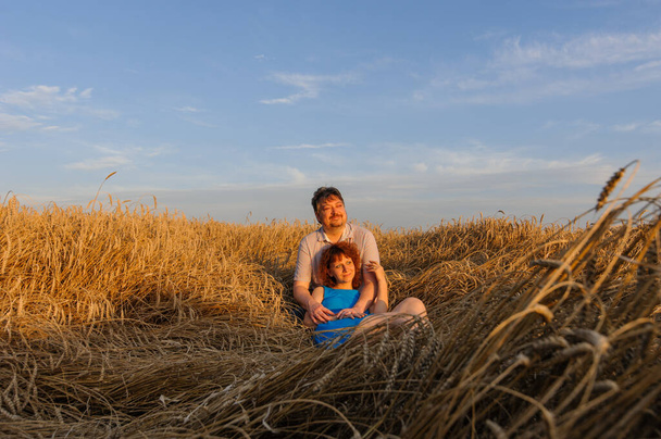 Un agriculteur adulte et sa femme passent du temps ensemble. Un couple est assis dans un champ de blé et regarde le coucher du soleil
. - Photo, image