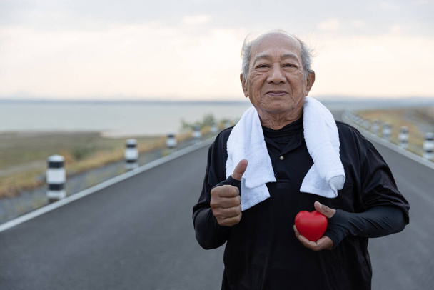 Азиатский старший мужчина в спортивной одежде держит красное сердце и много больших пальцев вверх. Концепция здравоохранения, здоровый с упражнениями и здоровое хорошее начало, страхование, мировой день сердца, медицинское страхование
 - Фото, изображение