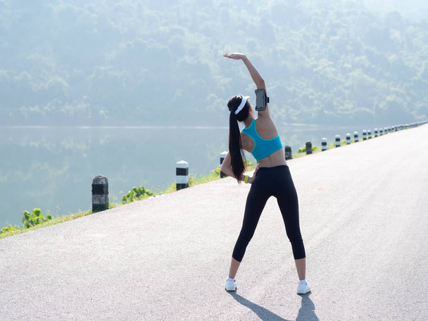 Rear view Young asian woman stretching arm muscles and preparing to running exercises on road in the morning sunshine.  Sportswoman, body slim, Health lifestyle Concept. with Copy Space - Photo, Image
