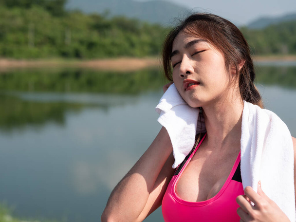 Nahaufnahme Eine junge Asiatin wischt sich den Schweiß von der Stirn, nachdem sie in der Morgensonne im Freien auf der Straße gelaufen ist. Joggerin beim Training. Fitness und gesunder Lebensstil - Foto, Bild