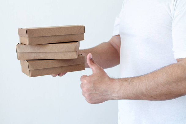 Чоловік з доставкою тримає картонні коробки в білій футболці. Кур'єрські руки крупним планом. Швидка і безкоштовна концепція доставки їжі. Експрес-доставка та онлайн-покупки. Карантинні будні
 - Фото, зображення