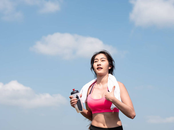 Ön tarafı kapatın. Genç Asyalı kadın sabah güneşinde yolda koşuyor. Kadın koşucu doğada şişelenmiş su tutarak egzersiz yapıyor. Fitness ve sağlıklı yaşam tarzı - Fotoğraf, Görsel
