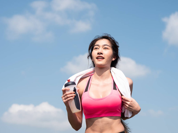 Ön tarafı kapatın. Genç Asyalı kadın sabah güneşinde yolda koşuyor. Kadın koşucu doğada şişelenmiş su tutarak egzersiz yapıyor. Fitness ve sağlıklı yaşam tarzı - Fotoğraf, Görsel