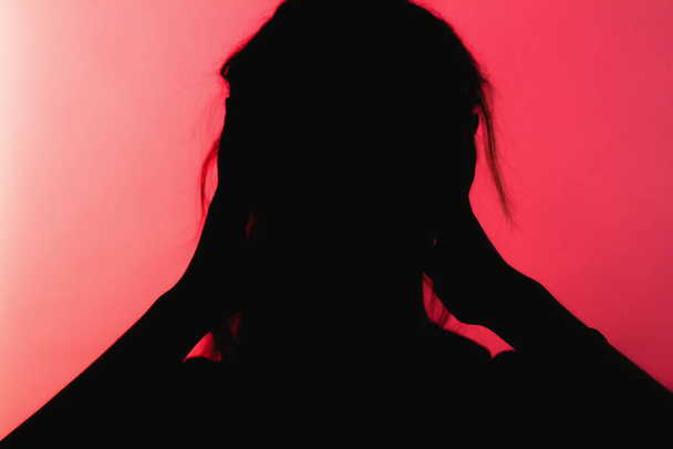 Silhouette eines besorgten Mädchens, das panisch die Hände hinter dem Kopf hält, unkenntliche Frau auf rotem Hintergrund, Konzept Lebensprobleme, Angst, destruktive Emotionen - Foto, Bild