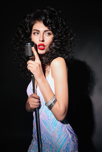 модна студія фото красивої сексуальної жінки з темним кучерявим волоссям в елегантній сукні позує з мікрофоном
 - Фото, зображення