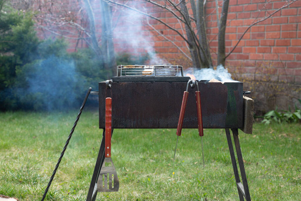 barbecue with smoke on a green lawn outside. red brick wall in the background. - Zdjęcie, obraz