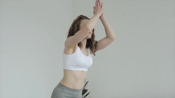 Beautiful young girl practices yoga while doing exercises and meditating at home standing on a mat in sportswear. Close-up - Filmagem, Vídeo