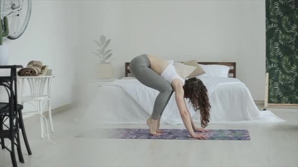Młoda atrakcyjna dziewczyna ćwiczy jogę przyjmując różne pozy stojąc na macie w swoim pięknym pokoju - Materiał filmowy, wideo
