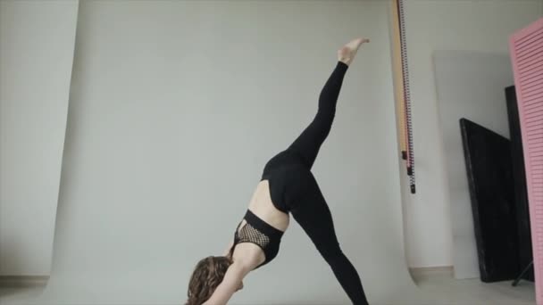 Beautiful young girl practices yoga while doing asana on a gray background in a black sports bra and black leggings - Footage, Video