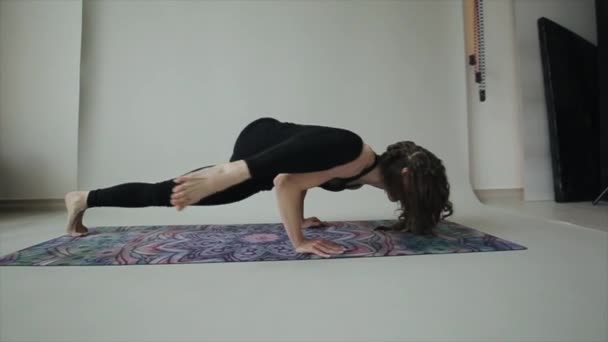 Young athletic girl practices yoga at home doing exercises one by one standing on the mat in a sports bra and leggings - Footage, Video