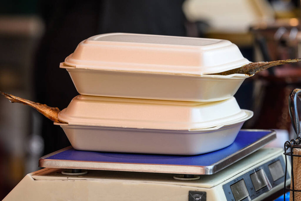 Dos cajas de plástico blanco para llevar con pescado fresco a la parrilla en una mesa en un mercado callejero de alimentos, listo para la venta y comer alimentos saludables
 - Foto, imagen
