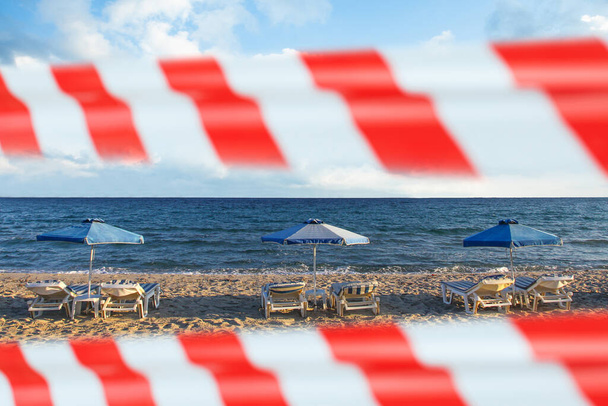 Uyarı bandıyla kapalı plaj. Kum, plaj şezlongu, şemsiye ve karantina yasağı. Gecikmeli tatil arkaplanı - Fotoğraf, Görsel
