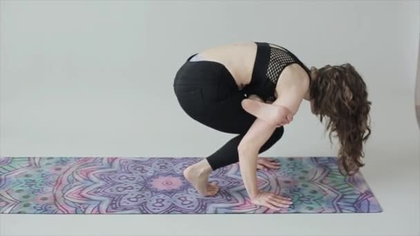 Genç atletik kız kompleks egzersizler yaparken yoga yapıyor ve siyah spor giysili bir paspasın üzerinde duruyor. - Video, Çekim