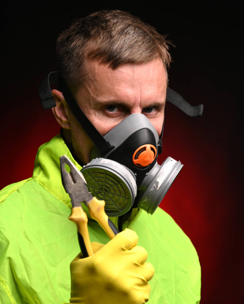 Mann mit Atemschutzmaske und Handschuhen hält Zange vor dunkelrotem Hintergrund - Foto, Bild