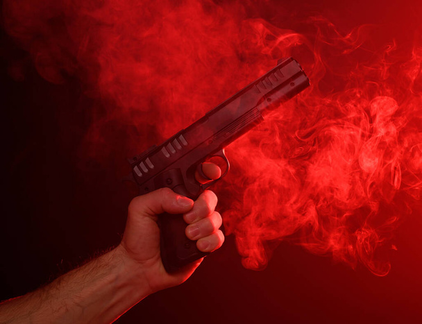 Mężczyzna trzymający broń na czerwonym dymnym tle - Zdjęcie, obraz