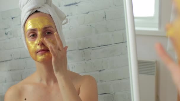 Frau trägt goldene Hydrogelmaske auf Gesicht auf - Filmmaterial, Video