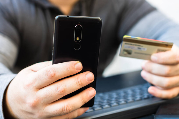 Mani in possesso di carta di credito e utilizzando smartphone e laptop. Shopping online, concetto di pagamento on line - Foto, immagini