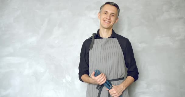 Portrait of a young smiling man worker or repairman in uniform holding a wrench against a gray background. - Video, Çekim