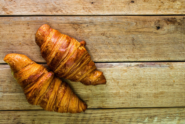 Detail of fresh croissant on wooden table. Food and breakfast concept. Top view and copy space - Photo, Image