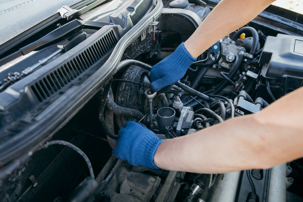Mavi eldivenli bir tamirci araba motorunu tamir ediyor. - Fotoğraf, Görsel