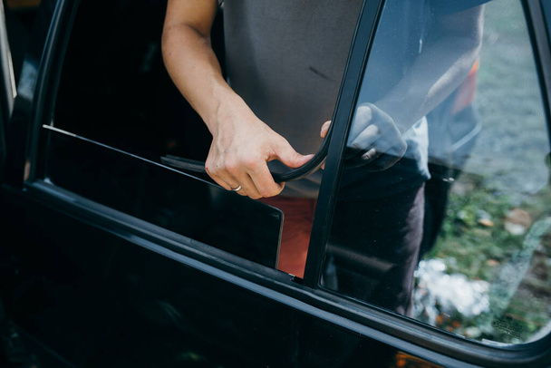 Um homem está mudando uma janela lateral de seu carro ao ar livre
.  - Foto, Imagem