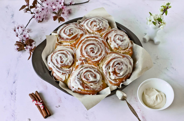 Cinnabon buns with cinnamon and creamy glaze, flowering twigs in a baking dish on a white background - Foto, Imagem